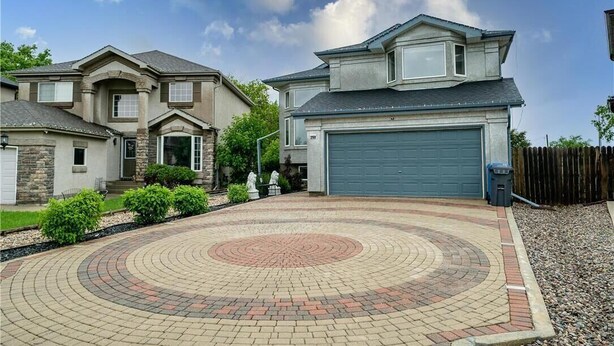 Une allée menant à une maison, avec un motif circulaire en briques qui aboutit à un garage.
