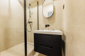 A modern bathroom with a glass shower enclosure, a white sink with black handles, and a mirror above the sink. - Beautiful Apartment - 1br/4p - Sentier (Paris)