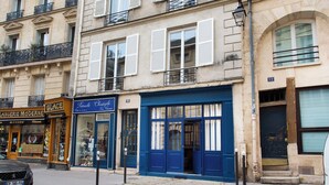 A street view with a building featuring a blue storefront, a visible number '12' on the facade, and a parked car. - Chic Apartment - 2br/6p - Pantheon (Paris)