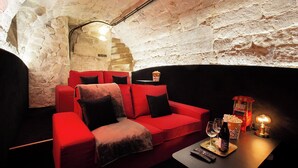 A cozy, stone-walled room with a red sofa, a small table with a bottle and glasses, and a popcorn bucket. - Chic Apartment - 2br/6p - Pantheon (Paris)