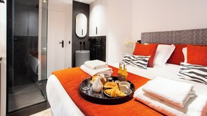 A hotel room with a bed, a glass shower enclosure, a breakfast tray with croissants and orange juice, and a large mirror. - Chic Apartment - 2br/6p - Pantheon (Paris)