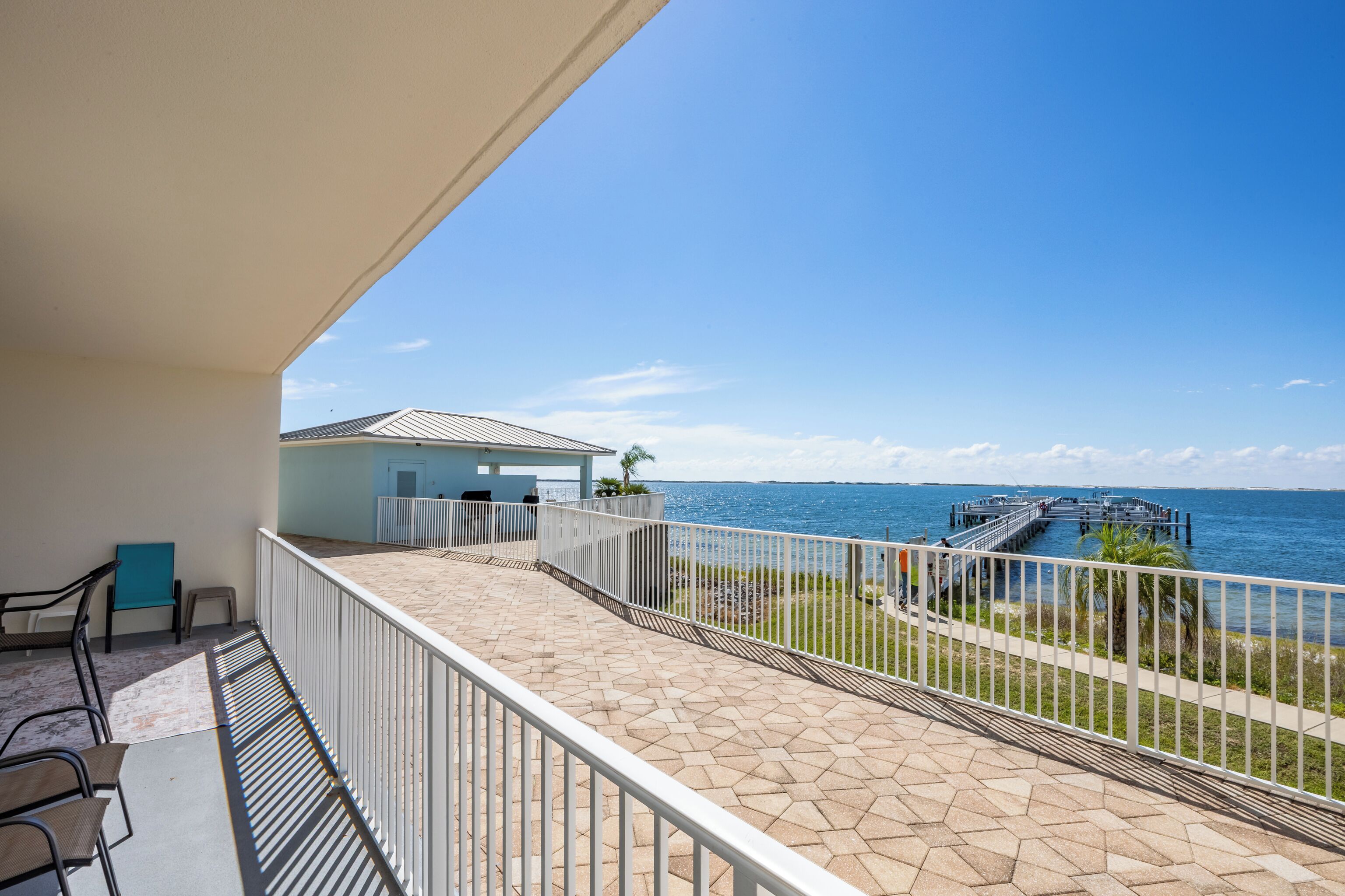 A balcony with a view of the sea, a small building, and a dock.