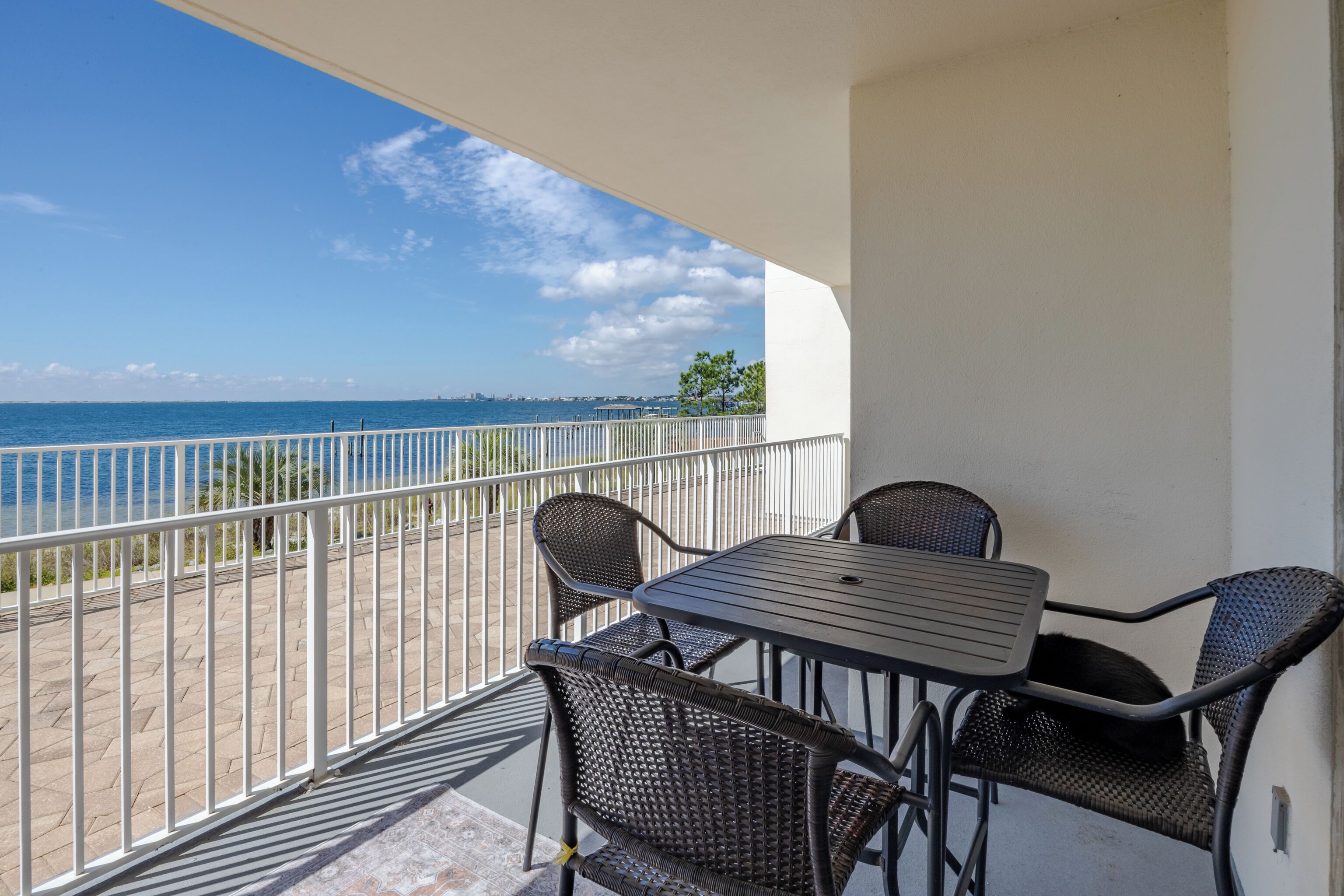 A balcony with a table and chairs, overlooking a beach and the sea.