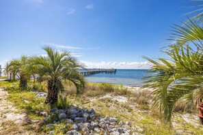 A beach with palm trees, a rocky path, and a pier extending into the water. - NEW WATERFRONT WITH GORGEOUS VIEW! (Pensacola)