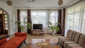 Sala de estar com sofá, televisão e duas plantas em vasos.