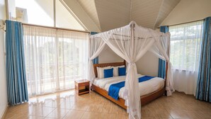 Quarto com cama de dossel, mesa de cabeceira de madeira e vista para árvores através de amplas janelas.