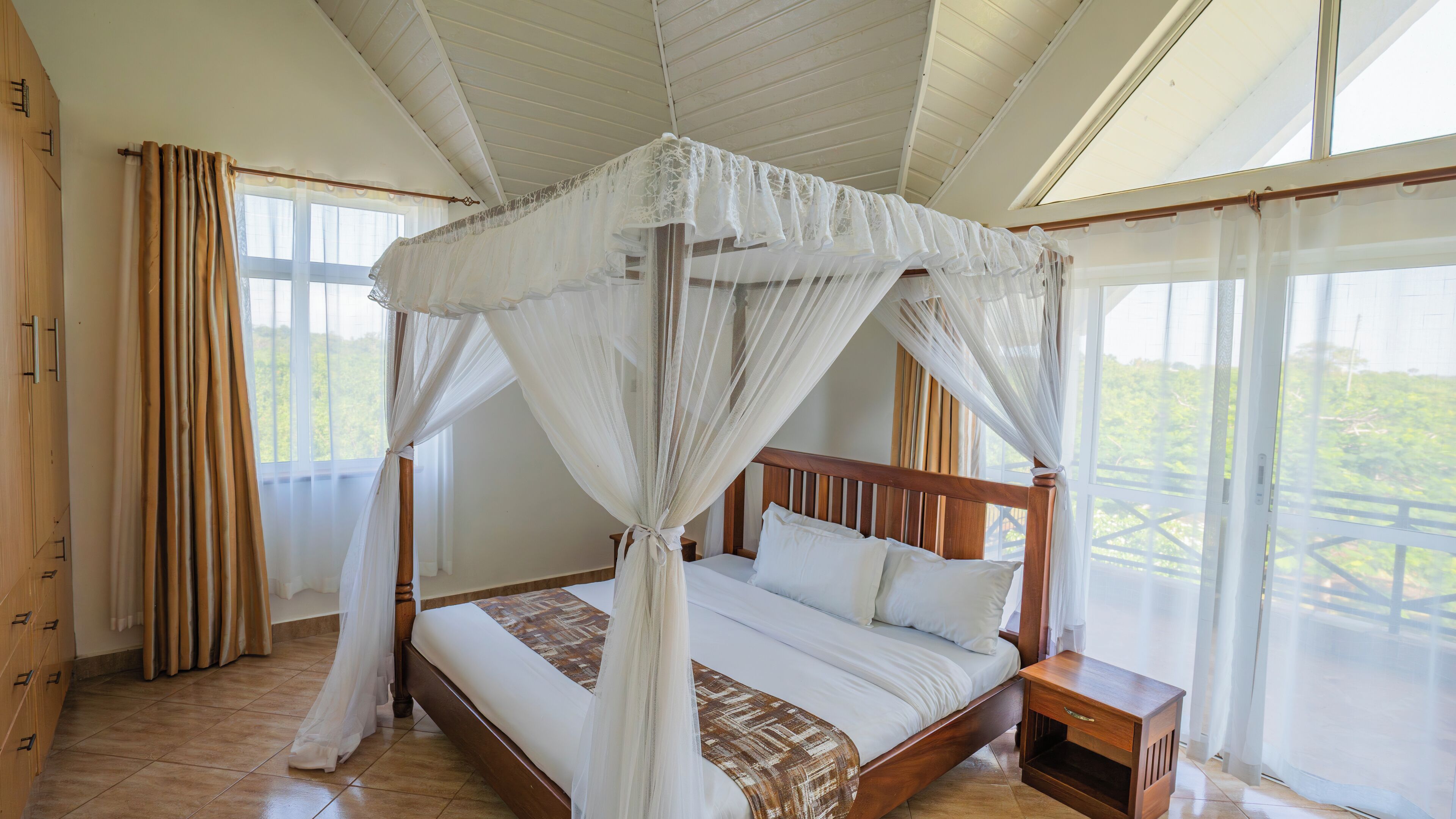 A four-poster bed with a canopy, wooden headboard, and a nightstand with a drawer.