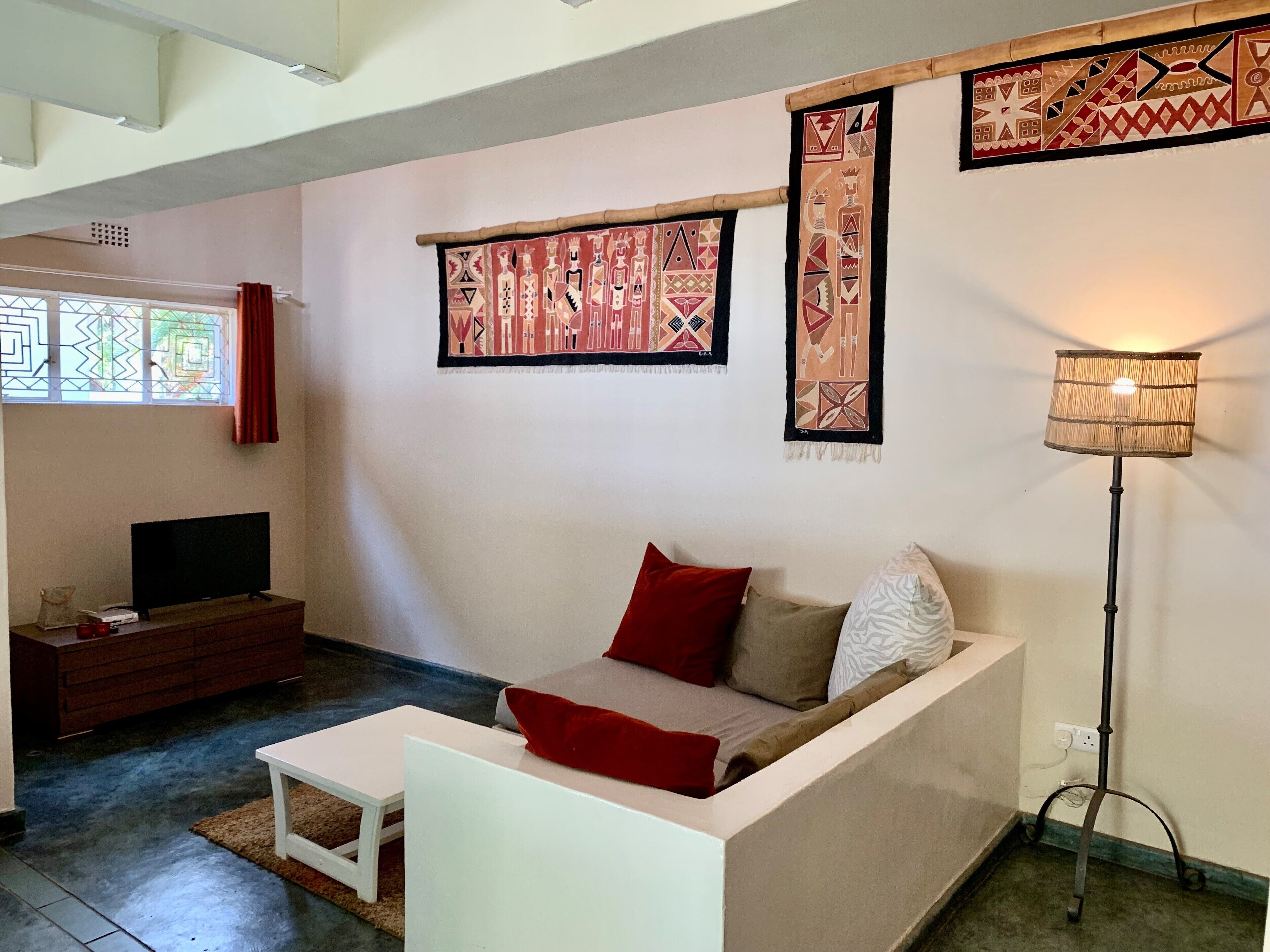 A living room with a sofa, a TV, a lamp, and decorative wall hangings.