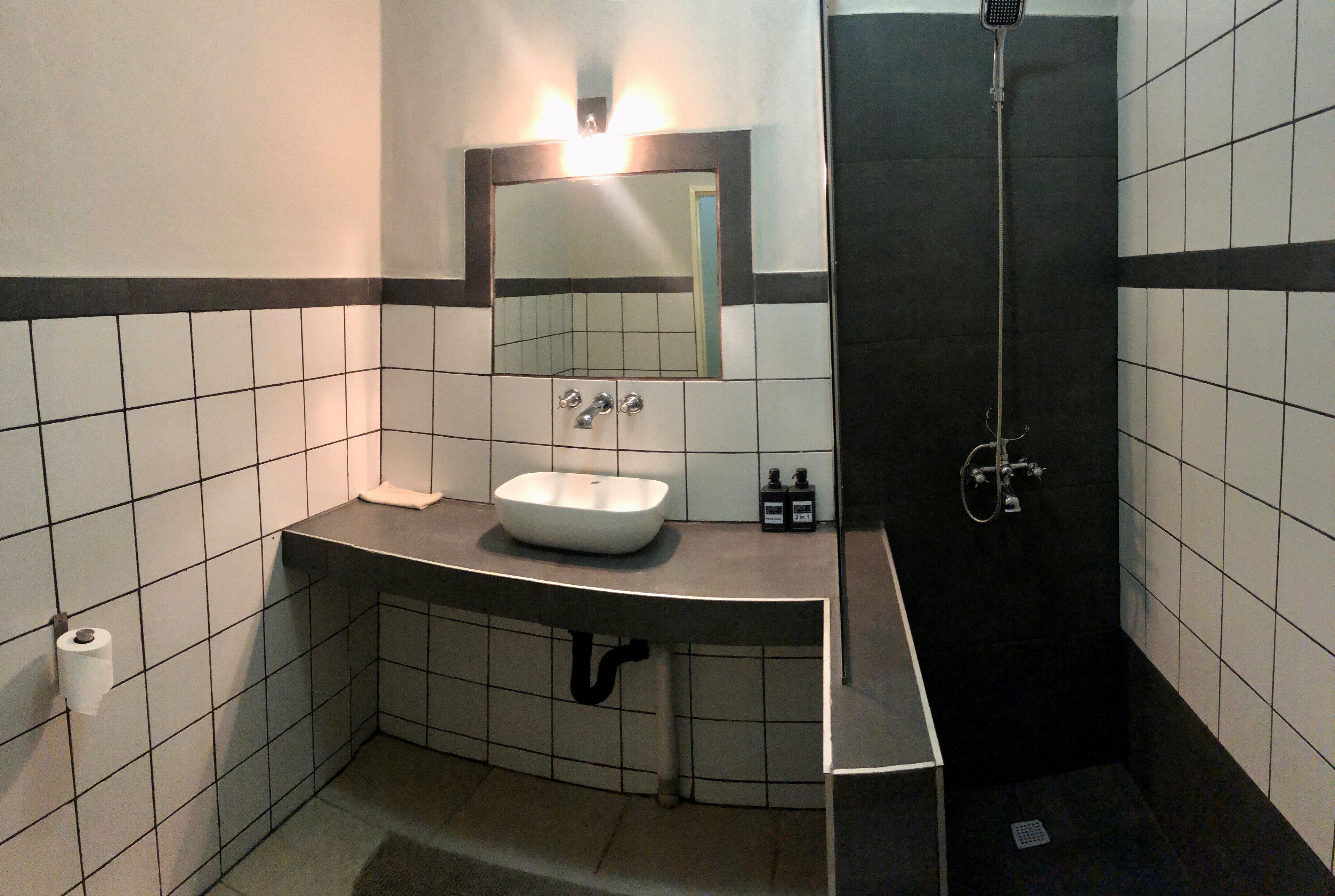 Une salle de bain avec un lavabo blanc, un miroir et des murs recouverts de carreaux noirs.