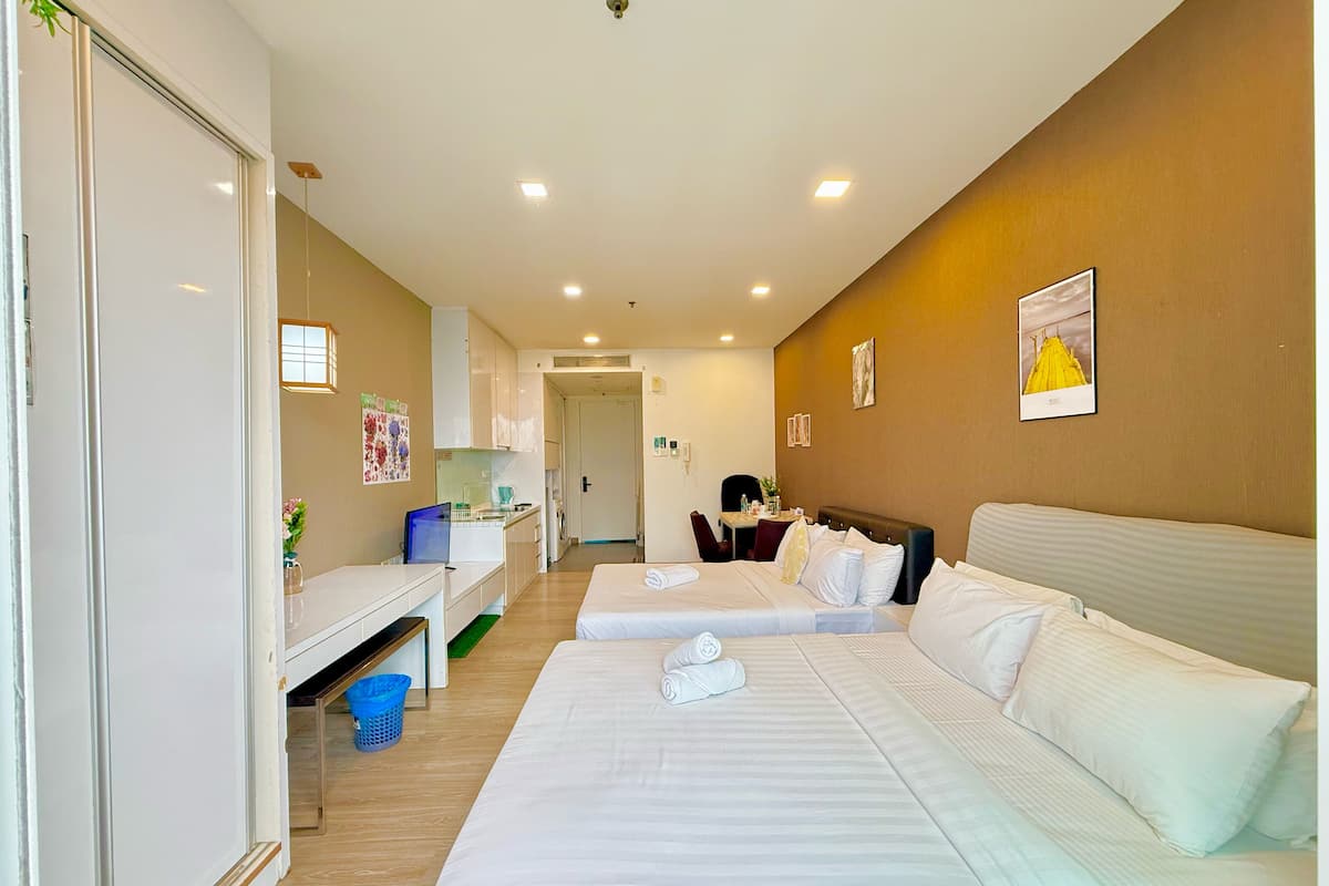 A hotel room with two beds, a desk, a chair, and a small kitchenette.
