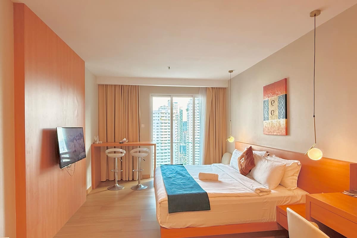 A hotel room with a bed, a desk, a TV, a window with a city view, and a painting on the wall.