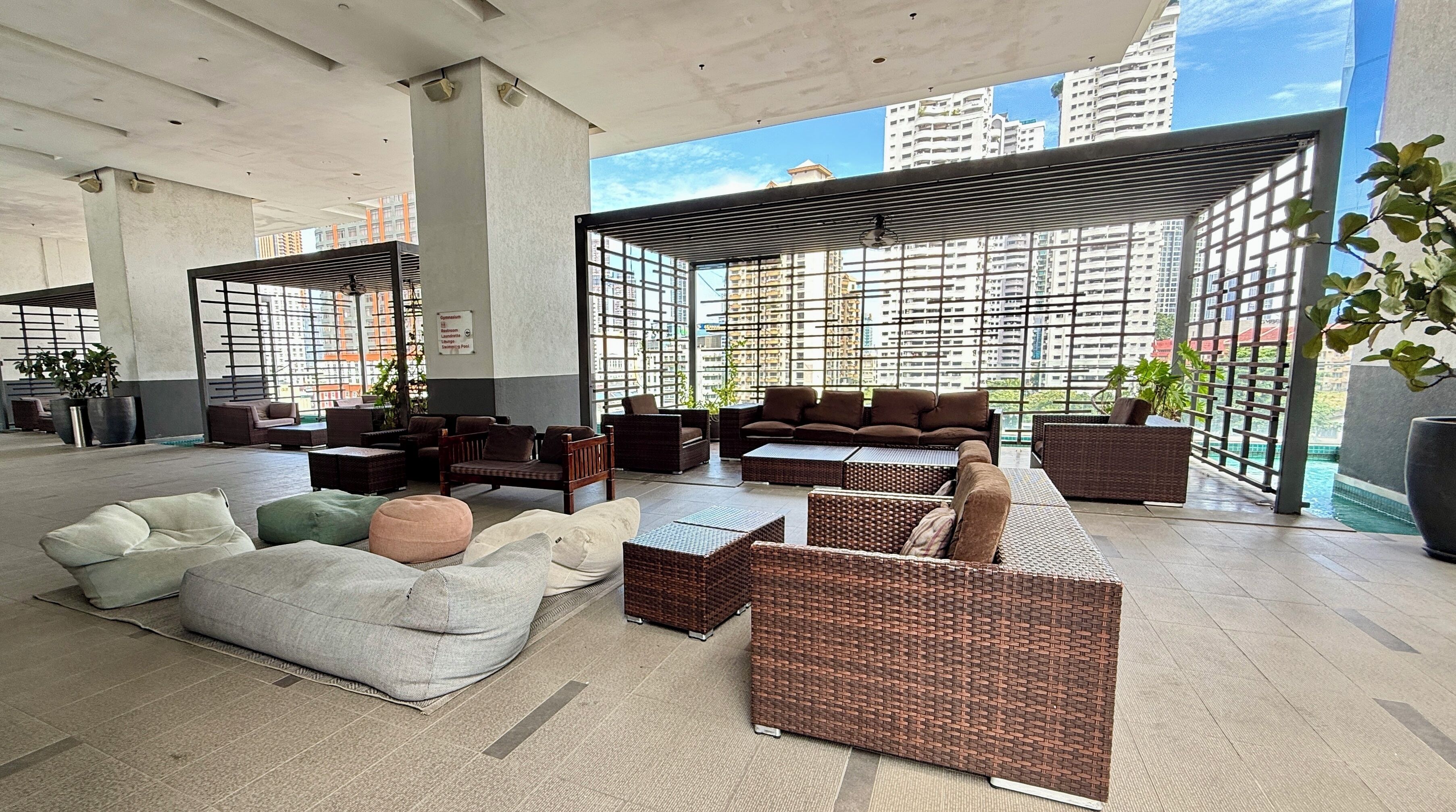 A spacious lounge area with modern furniture, large windows offering city views, and a high ceiling.