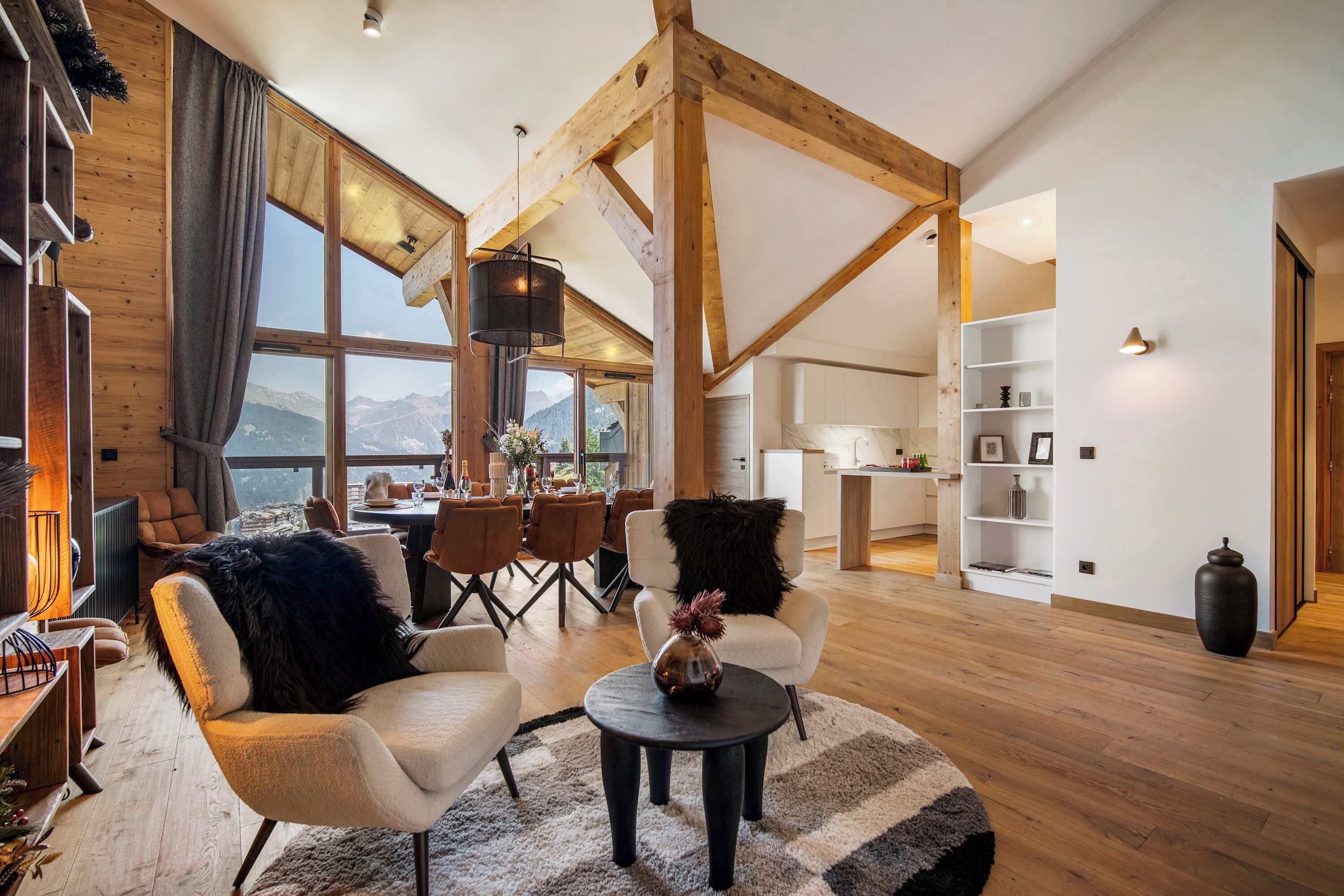 Amplia sala de estar con vigas de madera, un ventanal con vistas a la montaña, zona de comedor y cocina.