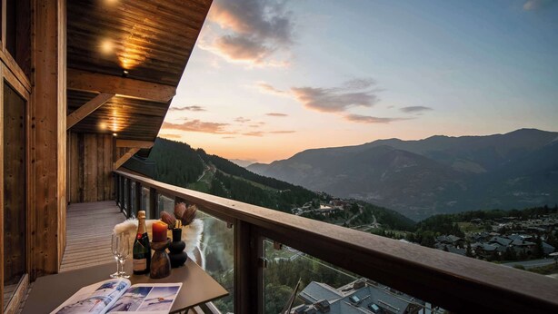 A wooden balcony with a view of mountains and a town below.