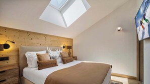A bedroom with a skylight, wooden headboard, a bed with white and brown bedding, a nightstand, and a wall-mounted light.