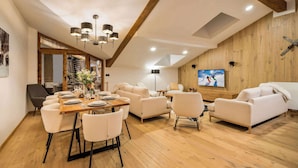 A spacious living area with a wooden floor, a dining table set for six, and a large flat-screen TV mounted on the wall.