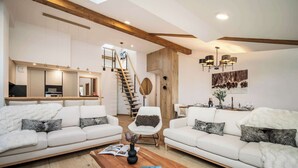 A spacious living room with two white sofas, a wooden coffee table, and a staircase leading to an upper level.