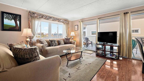 Un salon comprenant un canapé, des fauteuils, une table basse et un téléviseur. Il y a également un balcon avec vue sur la ville.