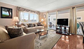 A living room with a sofa, armchairs, a coffee table, and a TV. There is a balcony with a view of the city. - Thunder Island 75B (Ocean City)