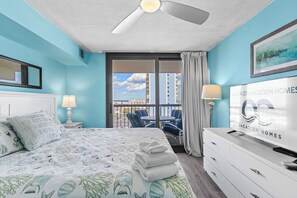 Ein Hotelzimmer mit Bett, Fernseher, Balkon mit Stühlen und Blick auf die Stadt.