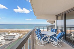 Ein Balkon mit Blick auf Strand und Meer, einem runden Tisch und gestreiften Stühlen.