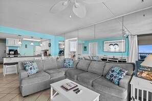 Una sala de estar moderna con un sofá seccional gris, una mesa de centro blanca y una cocina al fondo.