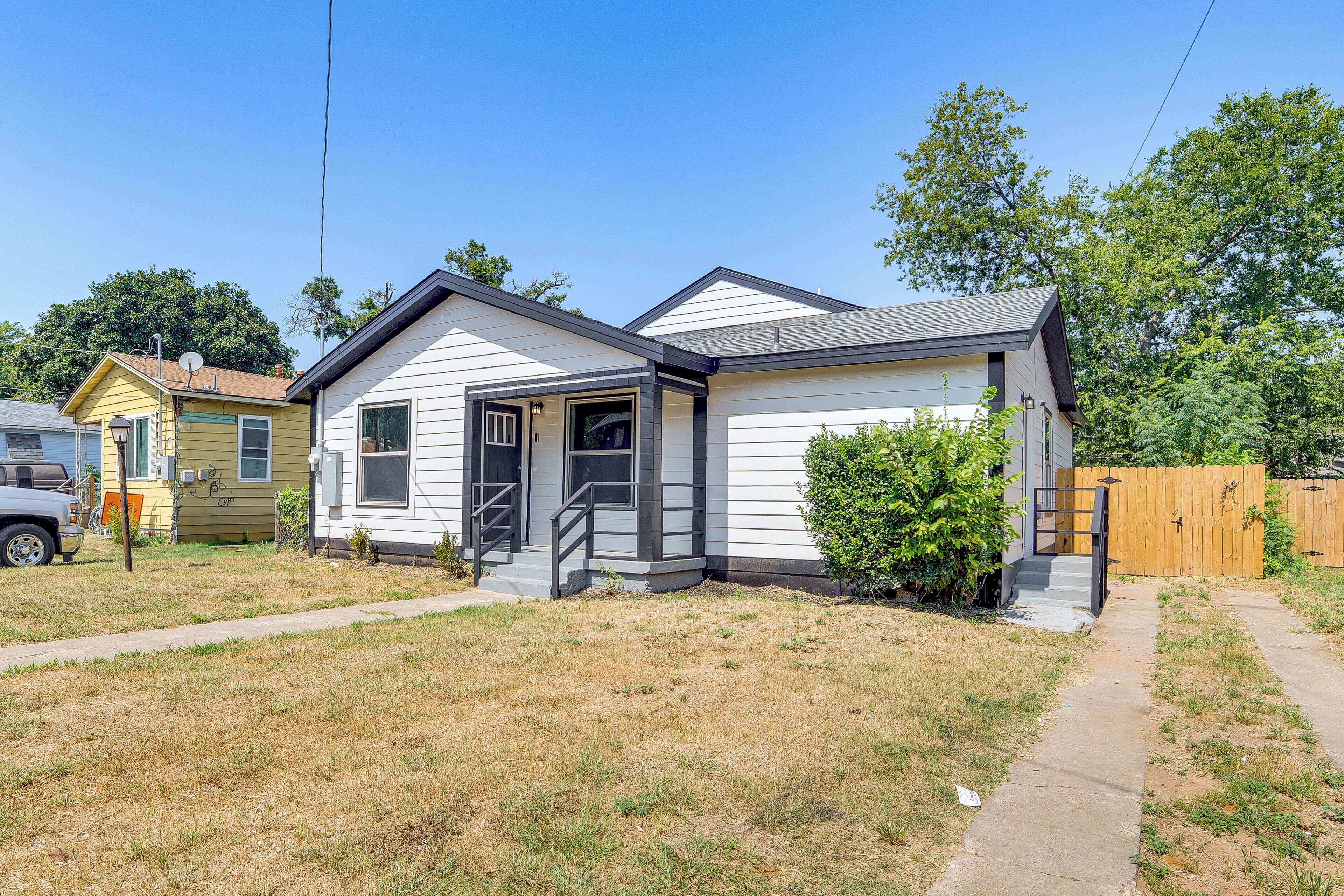 A single-story house with a front porch, a small front yard, and a wooden fence in the background.
