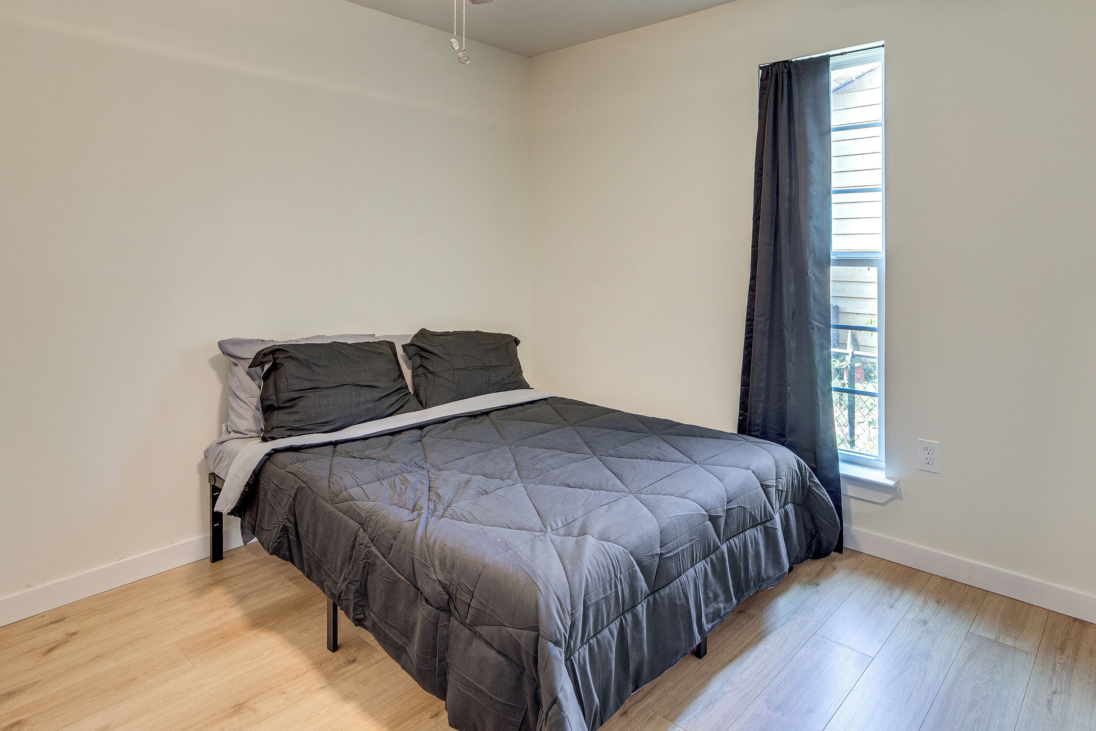 Ein Schlafzimmer mit einem Bett, einem Fenster mit Vorhängen und einem Lichtschalter an der Wand.
