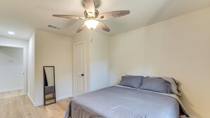 Een slaapkamer met een bed, plafondventilator, een deur en een spiegel.