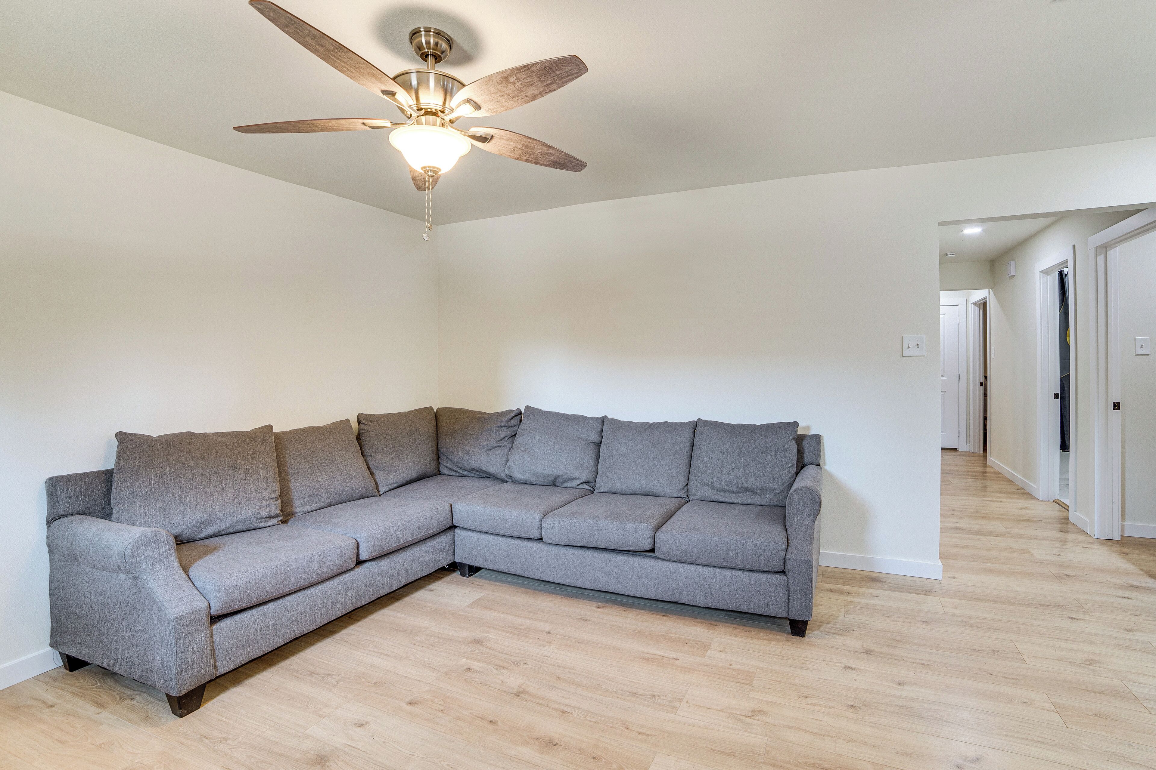 A modern living room with a grey sectional sofa, a ceiling fan, and a wooden floor.