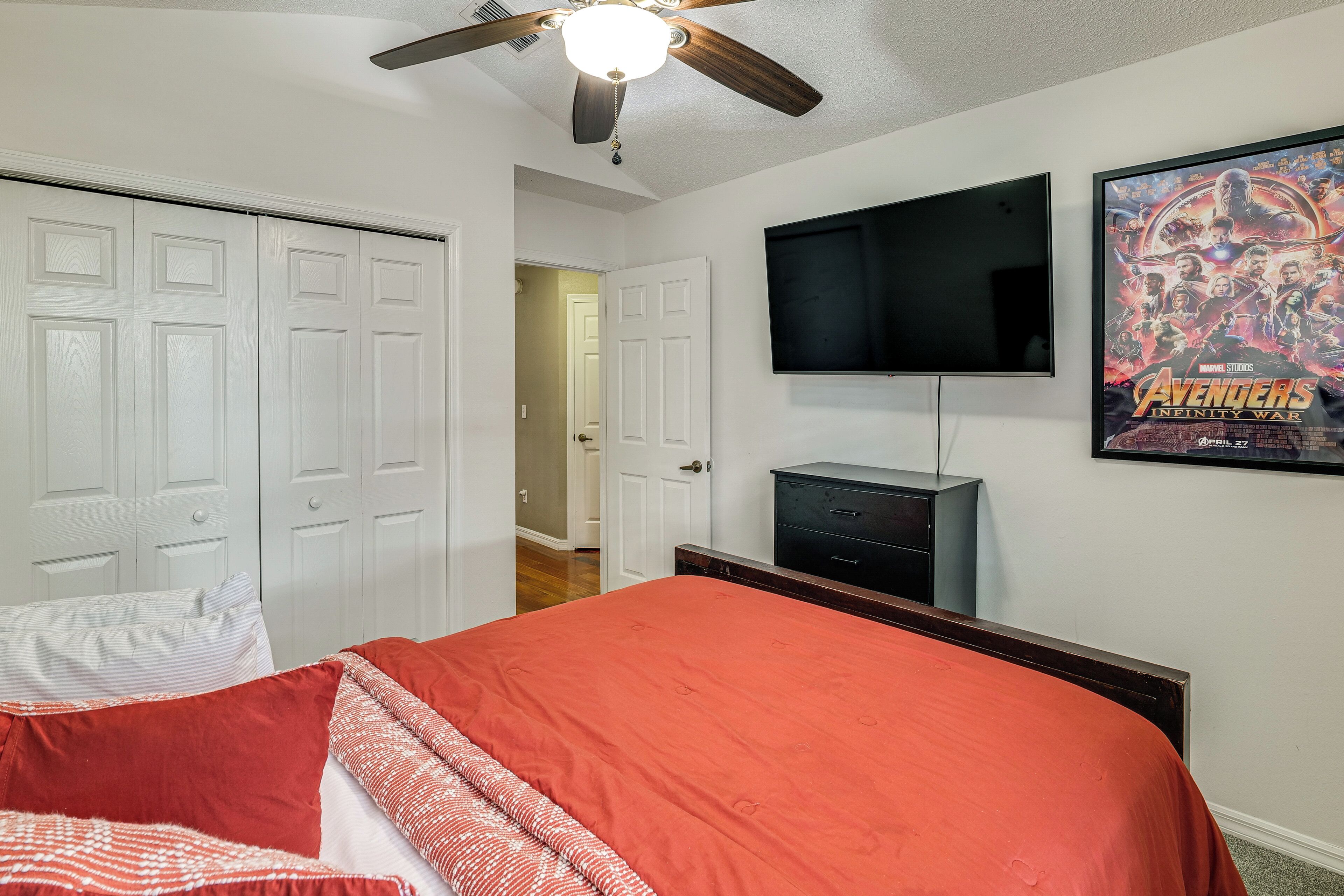 A bedroom with a bed, a ceiling fan, a TV, and a poster on the wall.