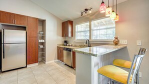 A modern kitchen with wooden cabinets, stainless steel appliances, a granite countertop, and a bar area with yellow chairs. - Large Yard: Home 9 Mi to San Antonio River Walk (San Antonio)