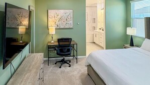 Un dormitorio con cama, escritorio, silla y un baño visible a través de una puerta abierta.