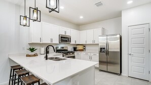Una cocina moderna con armarios blancos, un refrigerador de acero inoxidable y una isla central con taburetes.