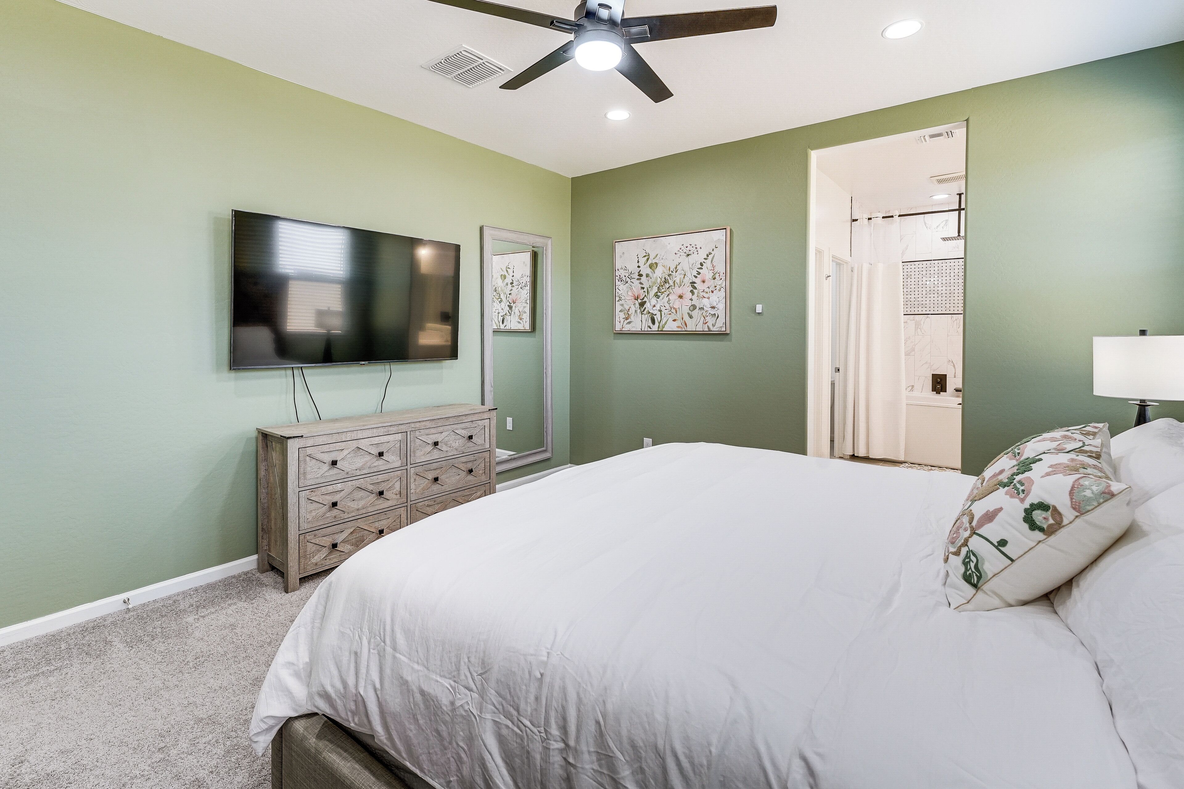 A bedroom with a bed, dresser, TV, and artwork on the walls.
