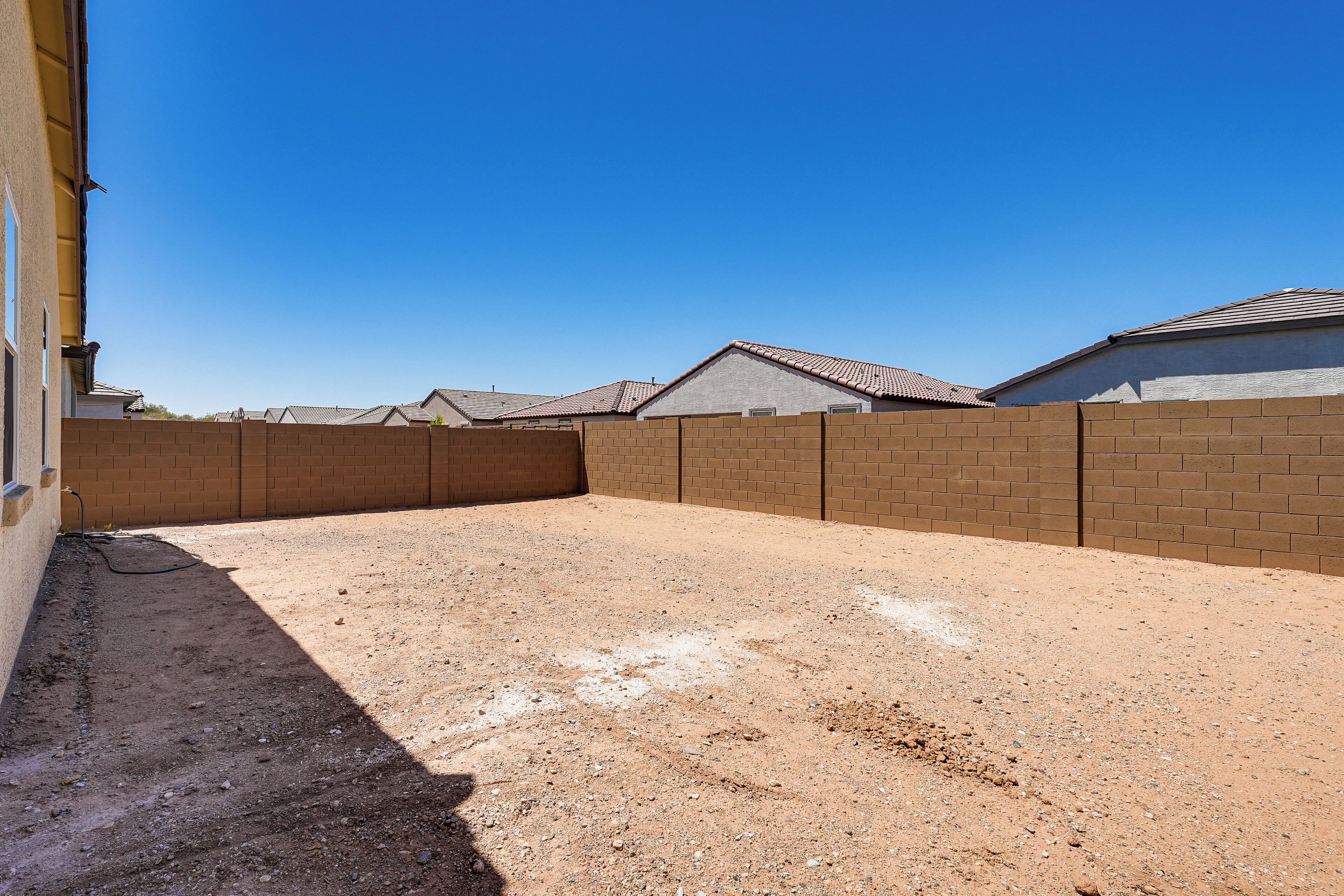 Patio trasero cercado con suelo de tierra, rodeado por muros de ladrillo y casas con techos de tejas.