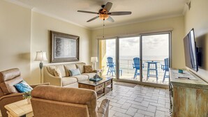 A living room with a sofa, armchairs, a coffee table, and a TV. There is a balcony with chairs and a table. - Direct Beach Access: NSB Condo w/ Community Perks (New Smyrna Beach)