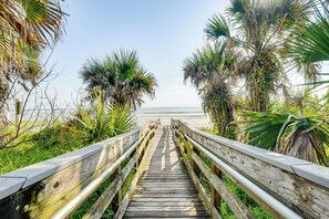 Una passerella di legno che conduce alla spiaggia, circondata da palme e vegetazione.