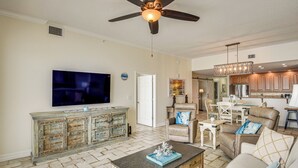 A spacious living room with a flat-screen TV, a ceiling fan, and a dining area with a chandelier. - Direct Beach Access: NSB Condo w/ Community Perks (New Smyrna Beach)