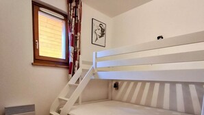 Une chambre avec un lit superposé, une fenêtre, un radiateur et un tableau accroché au mur.