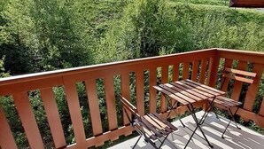 Une terrasse en bois avec une table et des chaises, offrant une vue sur un paysage verdoyant et luxuriant, avec des collines en arrière-plan.