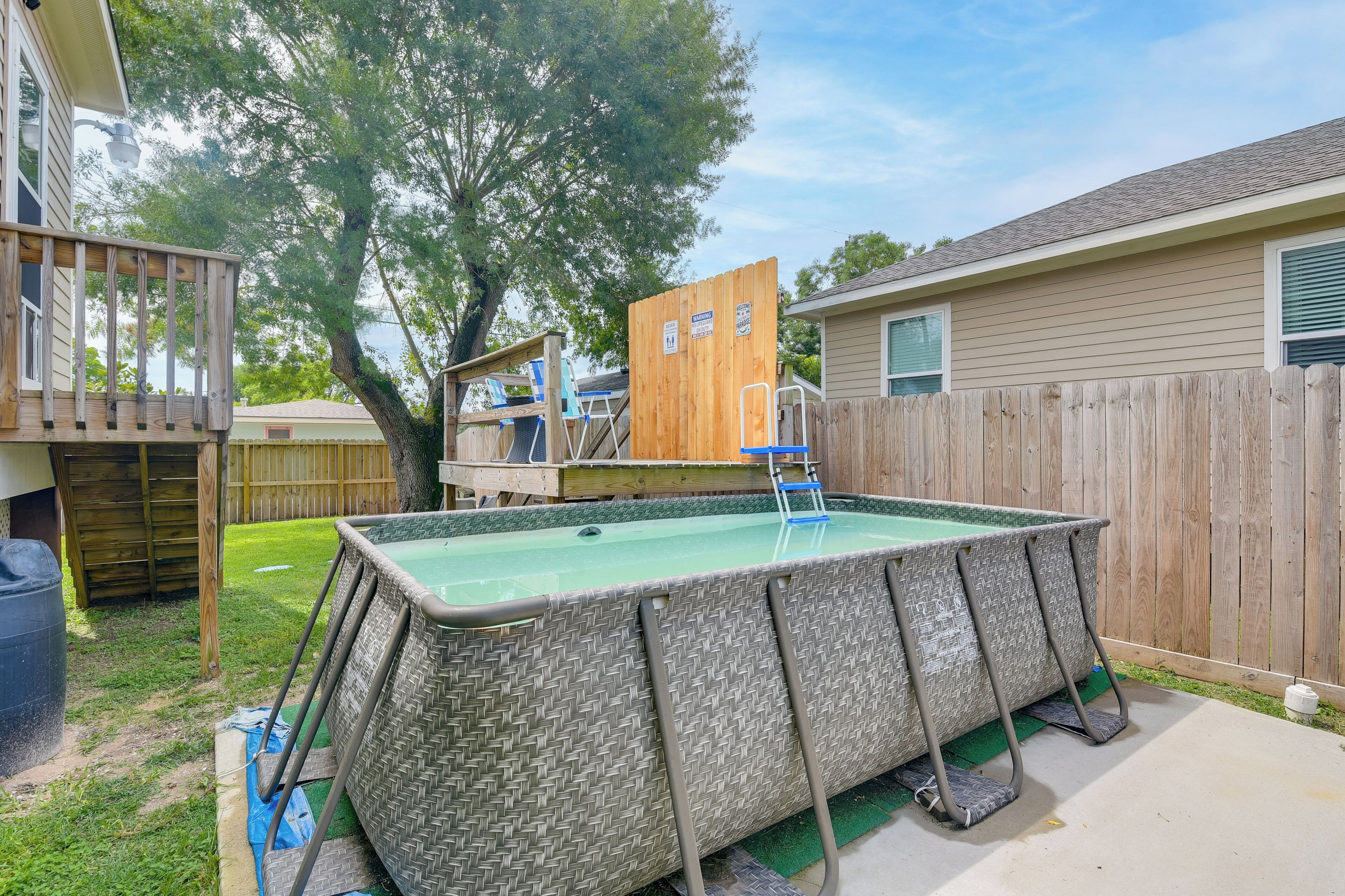 Un patio trasero con una piscina elevada rectangular, una terraza de madera y un área cercada.