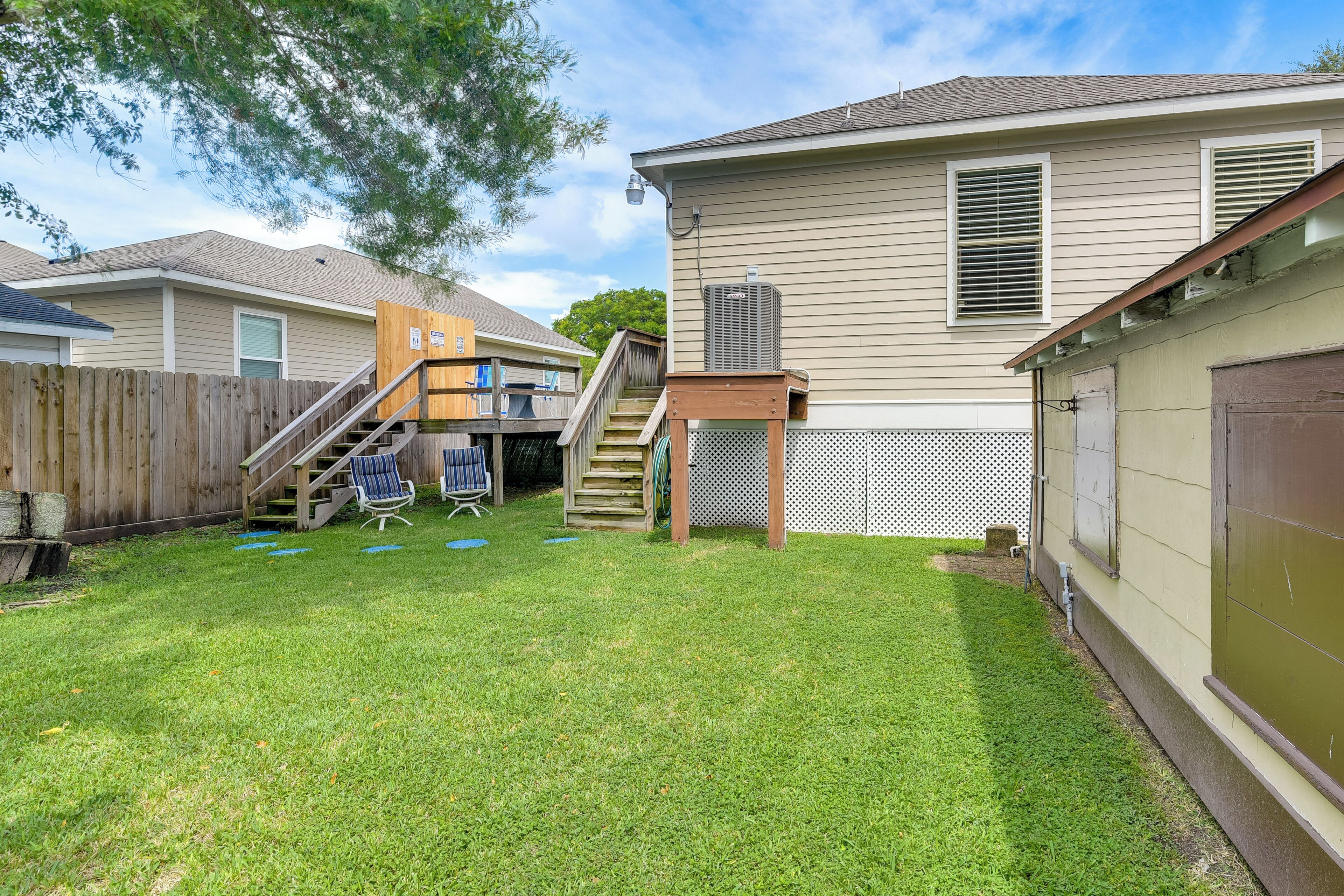 A residential backyard with a wooden deck, a small staircase, and a covered patio area.