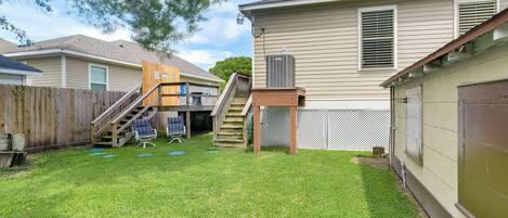 A residential backyard with a wooden deck, a small staircase, and a covered patio area.