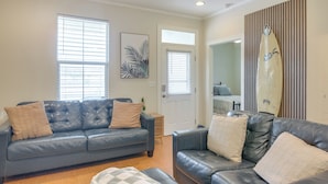 A living room with two dark leather sofas, a wooden floor, a door, and a surfboard on the wall.