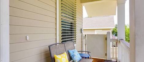 A porch with two chairs, one with a yellow pillow and one with a blue pillow, and a small table.