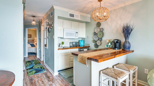 Una cocina compacta con armarios blancos, un microondas y una isla de madera con taburetes de bar.