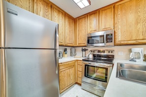 A kitchen with wooden cabinets, stainless steel appliances including a refrigerator, microwave, and oven, and a white countertop.