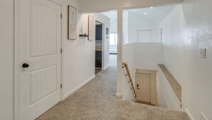 Un pasillo con una puerta blanca, una escalera con barandilla de madera y suelo cubierto de alfombra.