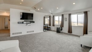 Un salón espacioso con un televisor de pantalla plana montado en la pared, un comedor con mesa y sillas, y ventanas grandes con cortinas.